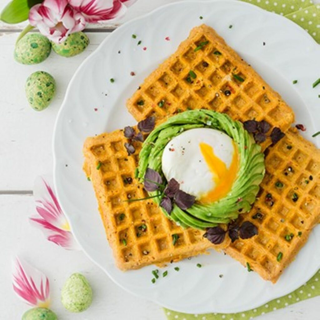 Oster-Waffeln mit pochiertem Ei und Avocado werden auf einem weißen Teller präsentiert.