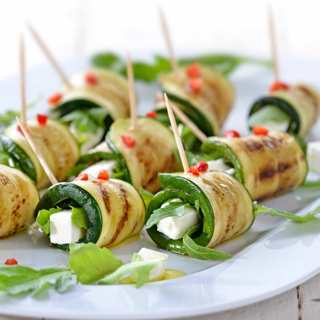 Zucchini-Röllchen mit Feta werden auf einem Teller mit etwas Rucola serviert.