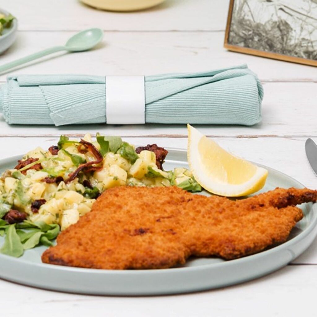Parmesanschnitzel wird mit Kartoffelsalat auf einem blauen Teller serviert.