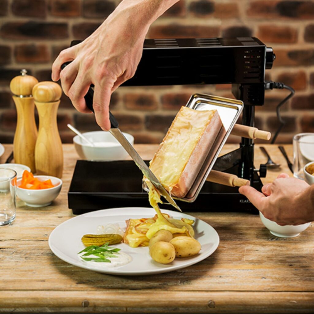 Walliser Raclette: Käse wird vom Grill auf Kartoffel geschabt.