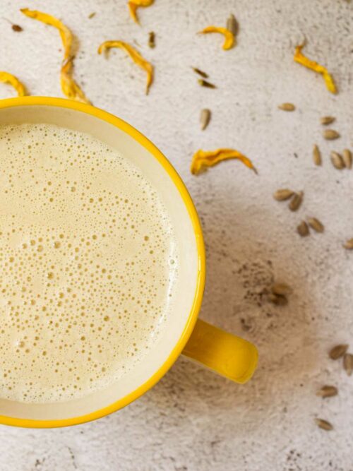 Sonnenblumenkernmilch wir in einer gelben Tasse mit ein paar Sonnenblumenkernen und -blüten gezeigt.