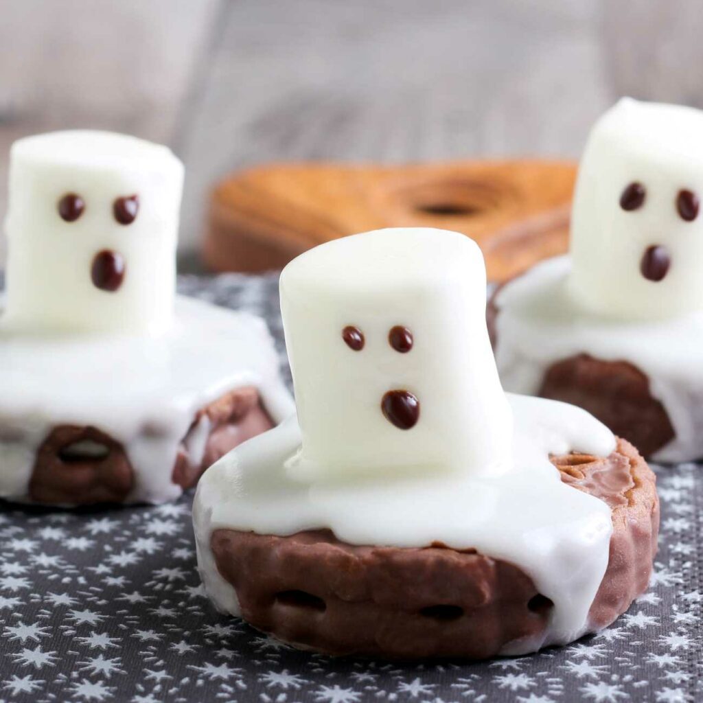 Halloween Cookies mit Marshmallow-Gespenstern werden auf einem blauen Untergrund gezeigt.