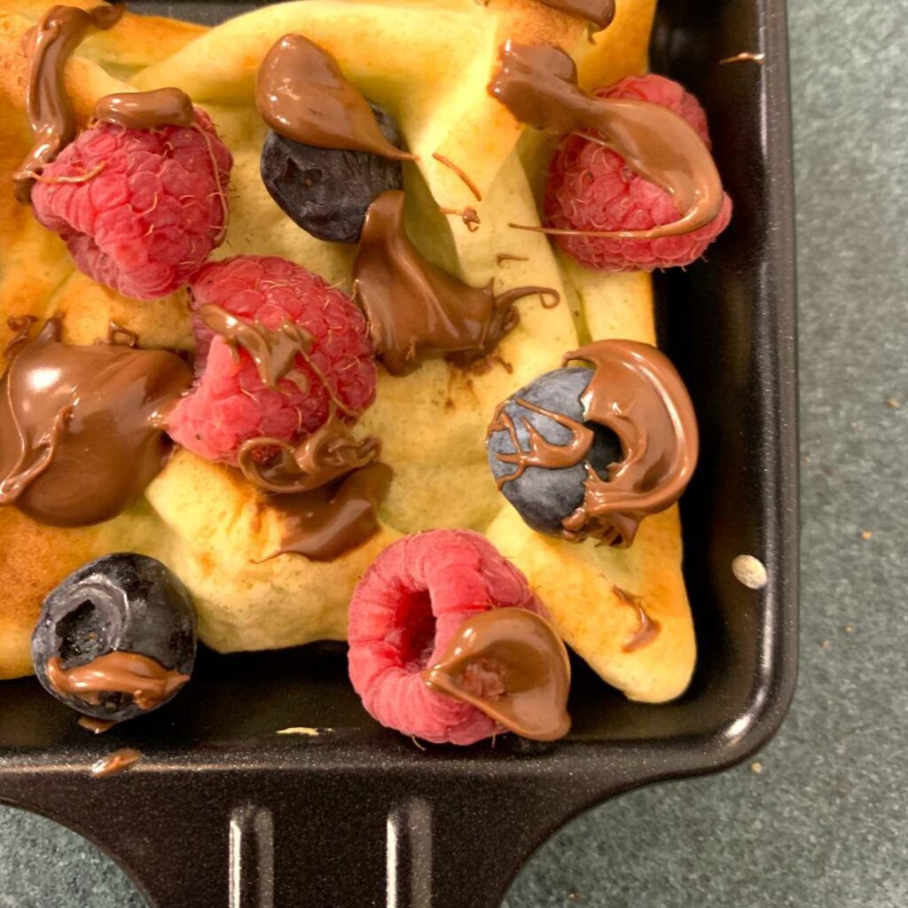 Crêpe-Raclette wird mit Beeren und Nutella im Pfännchen gezeigt.