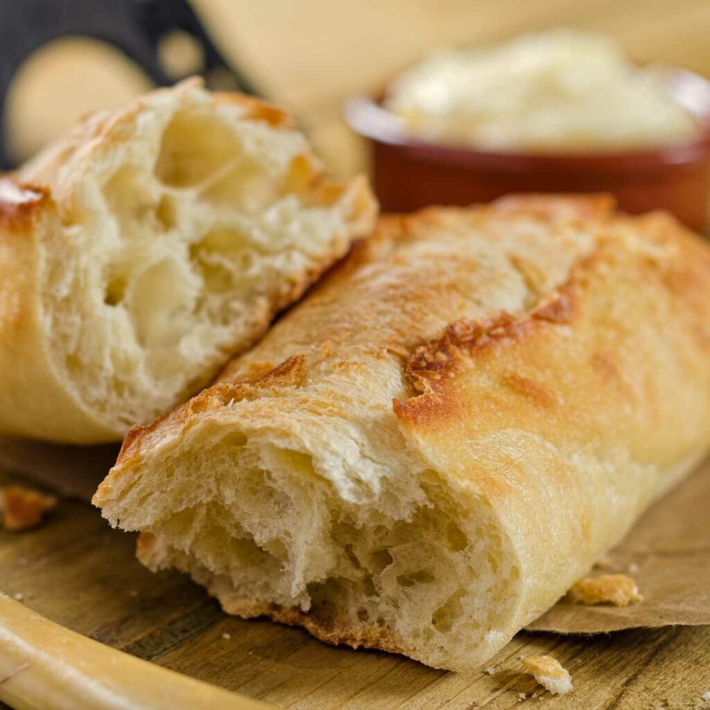 Original französisches Baguette wird angerissen auf einem Holzbrett gezeigt.