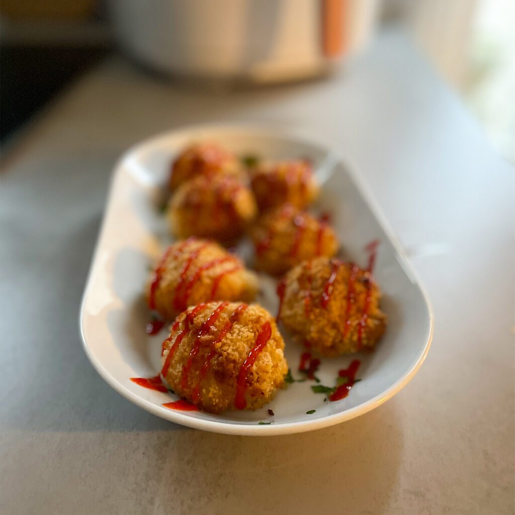 Gefüllte Kartoffelbällchen werden auf einem Teller mit Sriracha Sauce serviert.